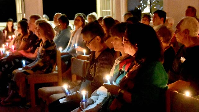 People sitting quietly, holding candles in a dimly lit room.