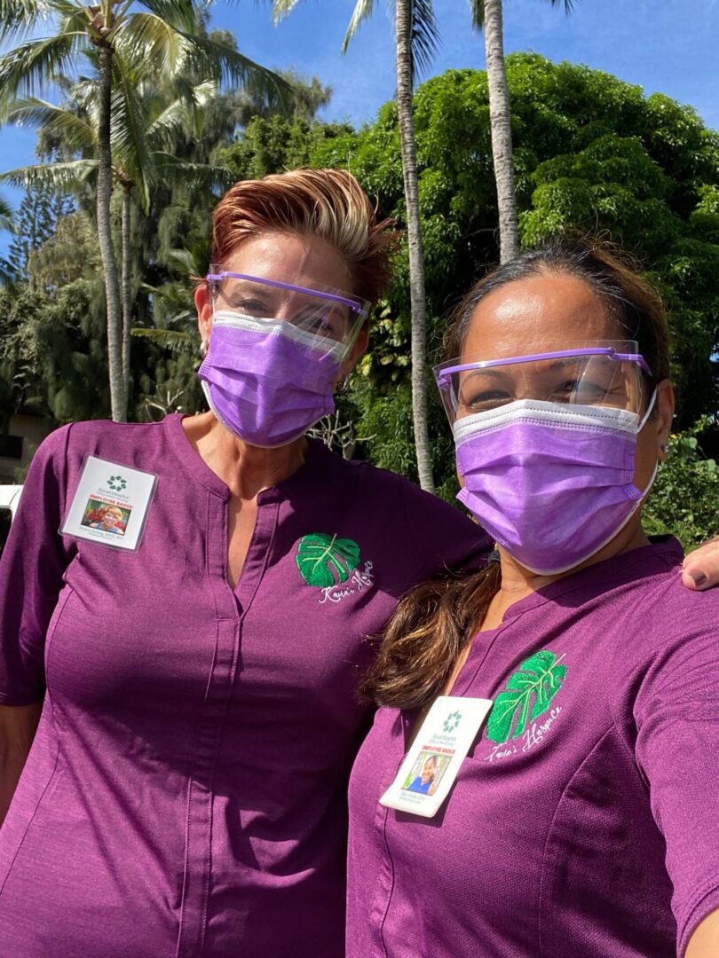 Two masked healthcare workers in purple scrubs