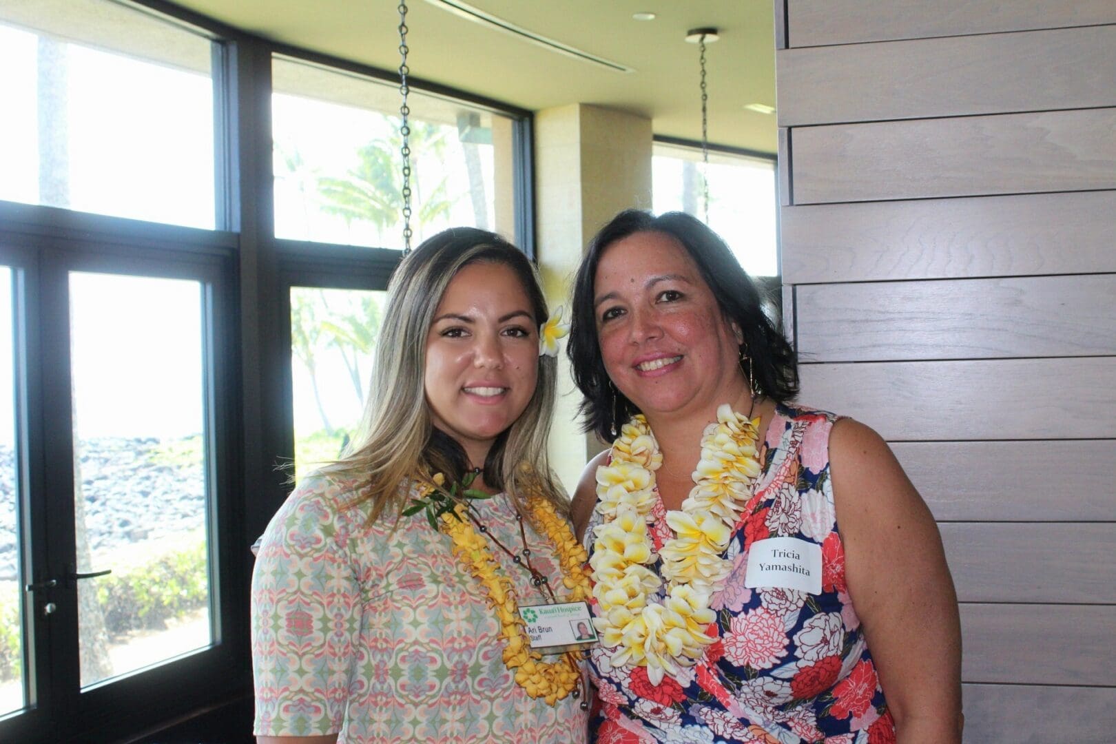 Two smiling women wearing leis by window